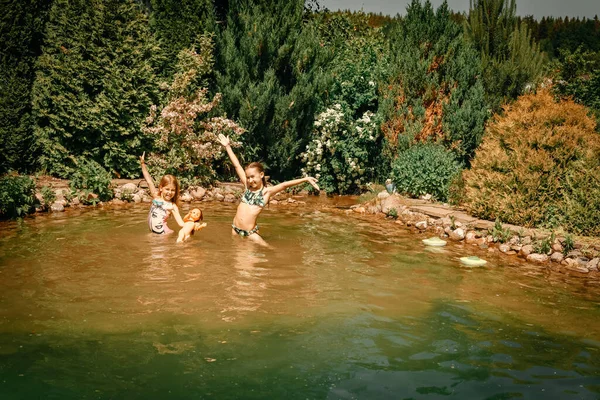 暑い夏の日にビキニの女の子2人が池で泳いでいます 幸せな子供たちは夏休みを楽しんでいます 湖で子供たちが入浴 — ストック写真