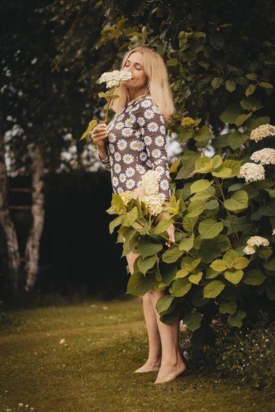 快乐的女人 金发碧眼 穿着白色的裙子 穿着夏天的毛衣 赤脚在公园里散步 女孩抱着鲜花在外面 快乐的女孩享受温暖的夏天天气 那姑娘在草坪上跑 — 图库照片