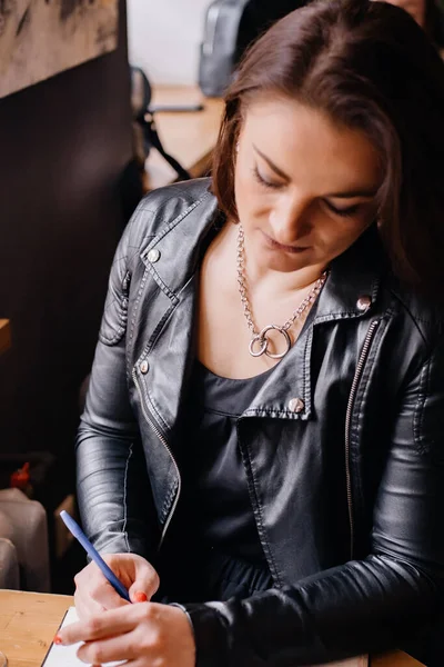 Portret Dziewczyny Skórzanej Kurtce Siedzącej Kawiarni Piszącej Coś Notesie Styl — Zdjęcie stockowe