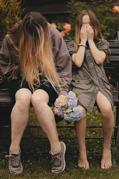 Две Красивые Молодые Девушки Длинными Волосами Позируют Скамейке Цветами Руках — стоковое фото