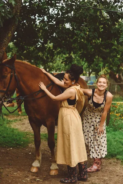 Dwie Samice Jeźdźców Długich Sukienkach Gumowe Buty Głaskające Brązowego Konia — Zdjęcie stockowe