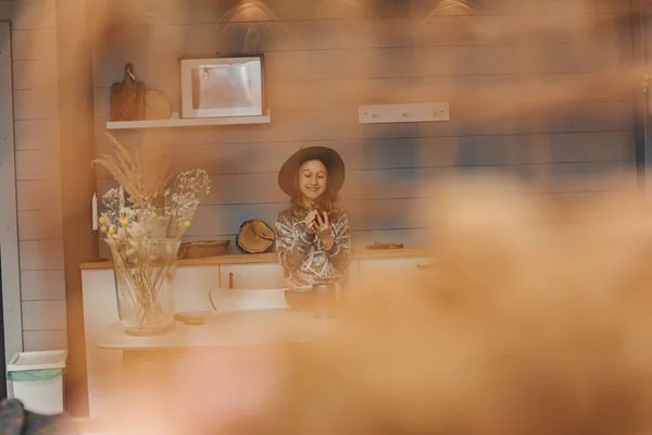 Hasır Şapkalı Küçük Bir Kız Elinde Telefonla Mutfakta Dikiliyor Mutlu — Stok fotoğraf