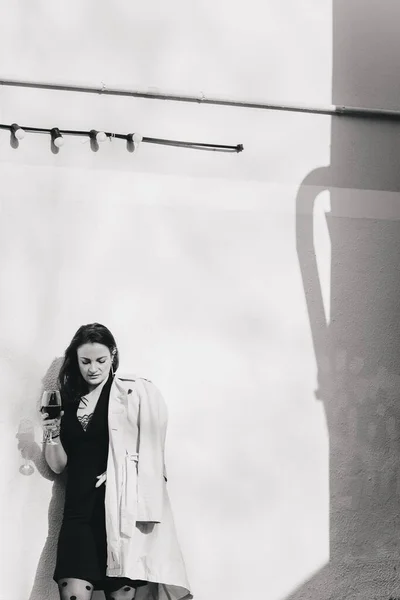 Siyah Elbiseli Trençkotlu Güzel Bir Kız Elinde Bir Bardak Şarapla — Stok fotoğraf