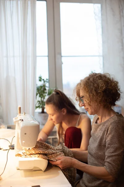ファッションデザイナーの2人の女の子がミシンで働いています 少女は家で服の縫製に従事している 創造的なプロセス 仕立て屋だ 縫製工房 — ストック写真