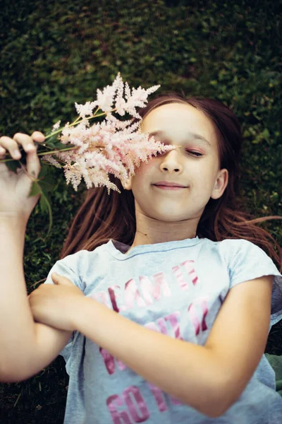 照片上的小女孩 一头乌黑的长发 双手捧着鲜花躺在草地上 一个在户外开着花的孩子的画像 有选择地集中注意力 分散注意力 调整语气 — 图库照片