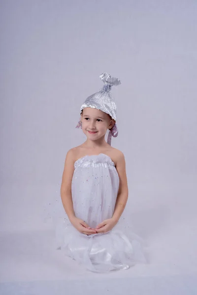 白いふわふわのドレスを着た可愛い女の子で 頭に銀の帽子を被った女の子が白い背景で小便をします 子供は白い背景に隔離されています — ストック写真