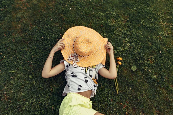照片来自上方 一个小女孩躺在公园的草地上 用一顶草帽盖住她的脸 在大自然中度过时光 公园里一个孩子的画像 有选择的重点 分散重点 — 图库照片