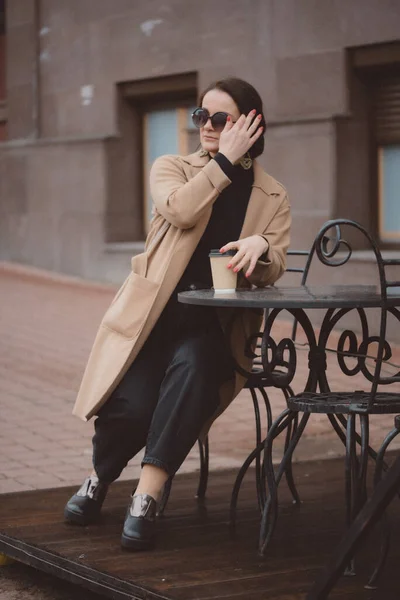 穿着防晒霜护目镜的时髦女人坐在咖啡厅阳台上喝咖啡的画像 街头时尚概念 — 图库照片