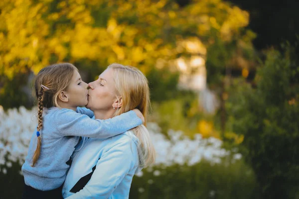 自然を背景にした少女と母親の肖像 母は路上で彼女の腕 抱擁とキスで娘を保持しています 愛とケアの概念公園で散歩のための彼女の娘と母 — ストック写真
