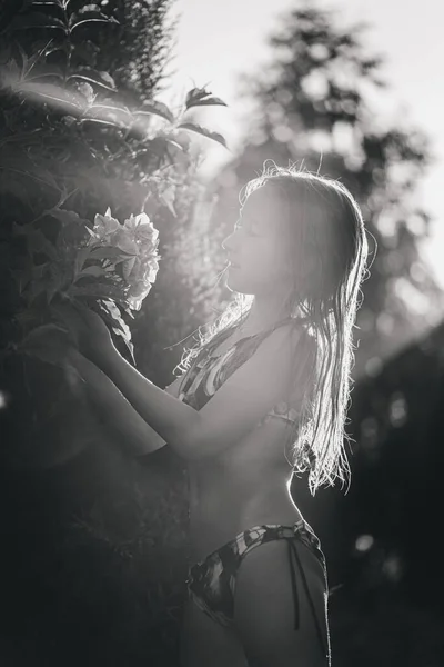 一个穿着泳衣的可爱小女孩喜欢花的芬芳 在夕阳西下的背景下 手里拿着一束白色的绣花 Toning 有选择的重点 分散重点 — 图库照片
