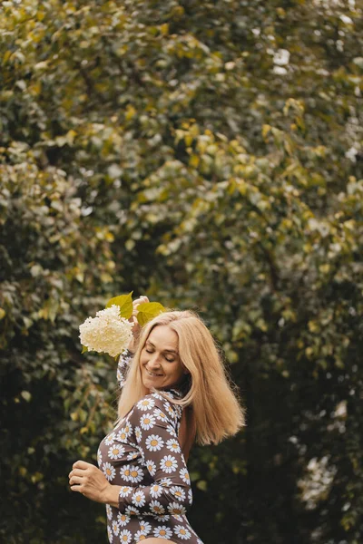 快乐的女人 金发碧眼 穿着白色的裙子 穿着夏天的毛衣 赤脚在公园里散步 女孩抱着鲜花在外面 快乐的女孩享受温暖的夏天天气 那姑娘在草坪上跑 — 图库照片