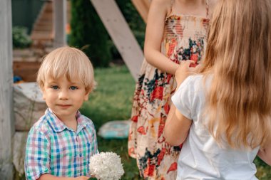 Portrait of a little boy with blond hair and blue eyes in a checkered shirt with a bouquet of flowers in his hands. Hydrangea flowers. Boy holding flowers outdoors. Selective focus, defocus.
