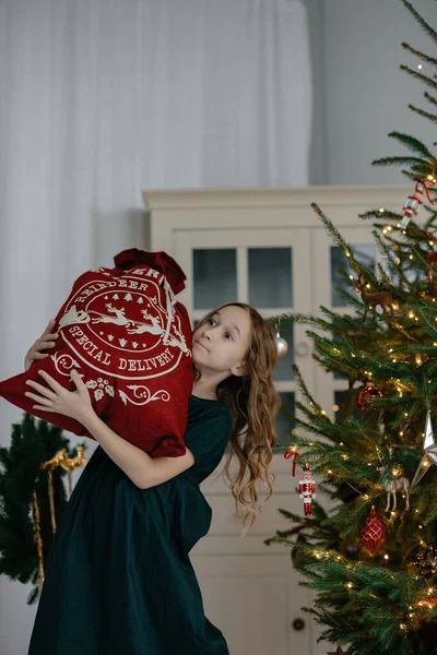 クリスマスツリーの手に贈り物の袋を持つ小さな女の子 新年の装飾付きの写真スタジオ クリスマスプレゼント 新年の広告 選択的フォーカス 子供は移動中だ — ストック写真