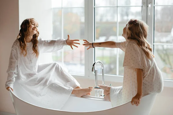 Két Fehér Pizsamás Kislány Egy Elegáns Fehér Fürdőkádban Ablak Mellett — Stock Fotó
