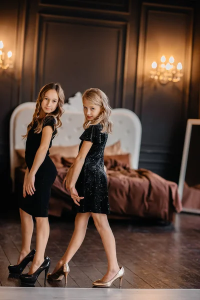 Zwei Hübsche Kleine Mädchen Schwarzen Kleidern Auf Mutters Fersen Posieren lizenzfreie Stockfotos