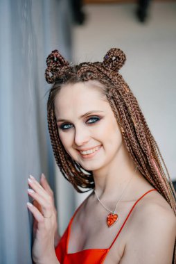 Yüzünde parlak makyajla ve kafasında saç örgüleriyle gülümseyen genç bir kız duvara dayanıyor. Afro örgülü bir kızın portresi. Tarz ve moda konsepti.