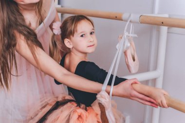 Şefkatli bir anne ve küçük kızı bale yapıyorlar. Eğitmen küçük bir kıza bale öğretiyor. Spor ve jimnastik konsepti. İki balerin. Pembe etekli küçük bir kız sanatla meşgul..