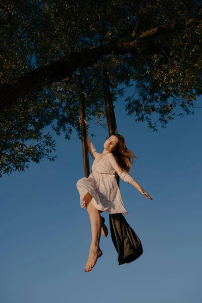 白いドレスを着た若い魅力的な女の子は 澄んだ空を背景に 木の近くの自然の中でスポーツをします 健康とスポーツの概念 空中体操 — ストック写真