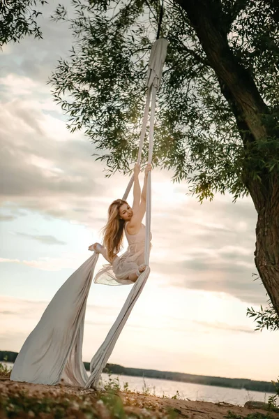 一位身穿白衣的年轻貌美的姑娘在清澈的天空背景下 在树旁的大自然中游玩 健康和体育概念 空中体操 — 图库照片