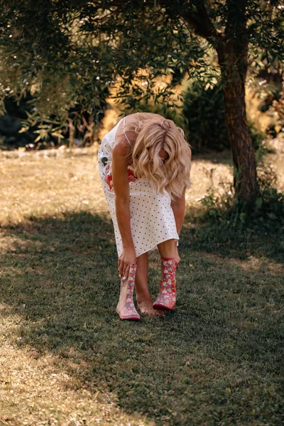 一个漂亮的女人 金发卷曲 穿着一条长长的白色围裙 穿着粉红色的橡胶靴 站在室外 — 图库照片