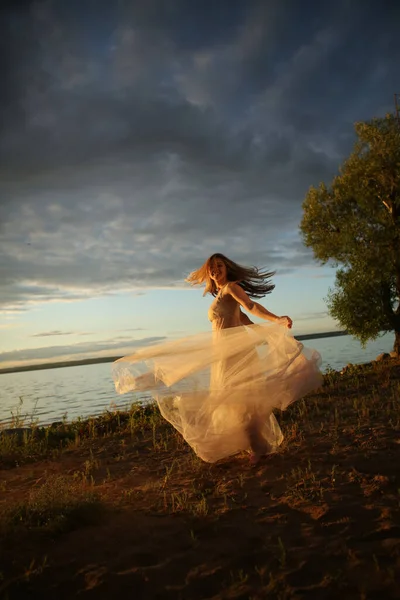 日落时 美丽的金发姑娘穿着漂亮的白色连衣裙在海滨 一位女士沿着海滨散步 背景是明亮的蓝色长方形 幸福和放松的概念 — 图库照片