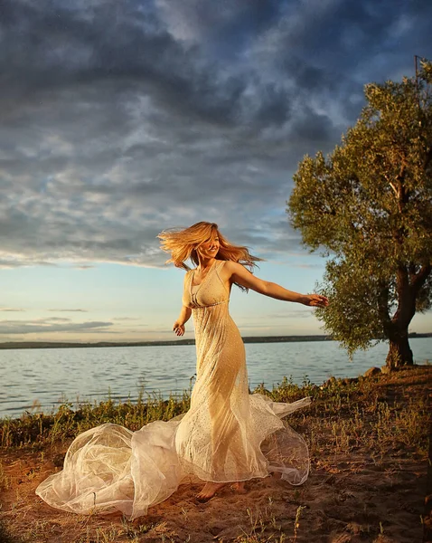 日落时 美丽的金发姑娘穿着漂亮的白色连衣裙在海滨 一位女士沿着海滨散步 背景是明亮的蓝色长方形 幸福和放松的概念 — 图库照片