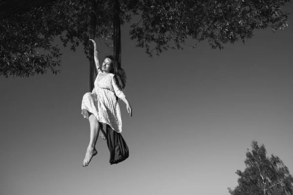一位身穿白衣的年轻貌美的姑娘在清澈的天空背景下 在树旁的大自然中游玩 健康和体育概念 空中体操 — 图库照片