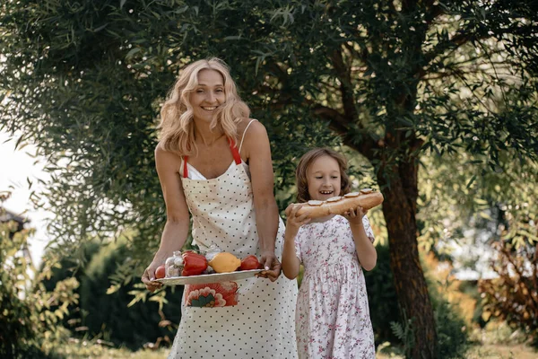 木の背景に果物や野菜を手に白いドレスを着た少女と彼女の母親 自然の中で夏のピクニック 母と娘は公園で一緒に楽しんでいます — ストック写真