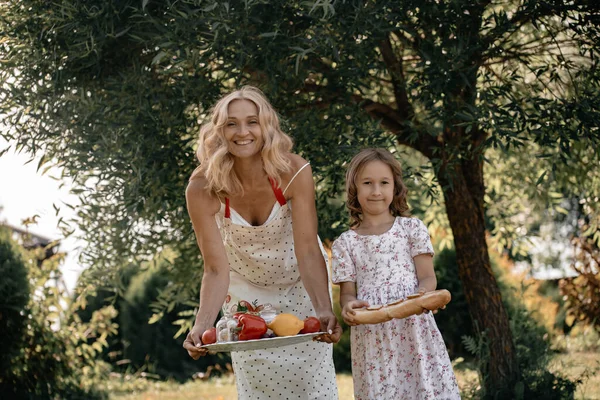 木の背景に果物や野菜を手に白いドレスを着た少女と彼女の母親 自然の中で夏のピクニック 母と娘は公園で一緒に楽しんでいます — ストック写真