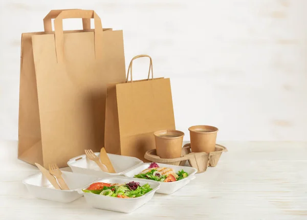 Entrega de comida. Bolsas de papel, loncheras con ensalada y café sobre fondo de madera blanca. Copiar espacio. — Foto de Stock