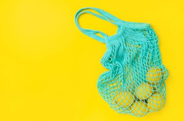 Lemons in reusable bag on yellow background. Overhead, copy space