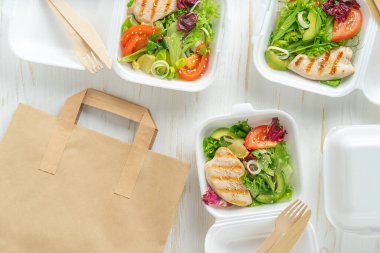 Beslenme çantaları ve kağıt torba beyaz ahşap arka planda. Yemek dağıtımı, üst görünüm, kopyalama alanı.