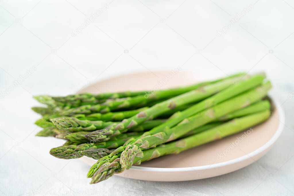 Heap of raw asparagus on plate on gray background. Healthy eating, copy space.