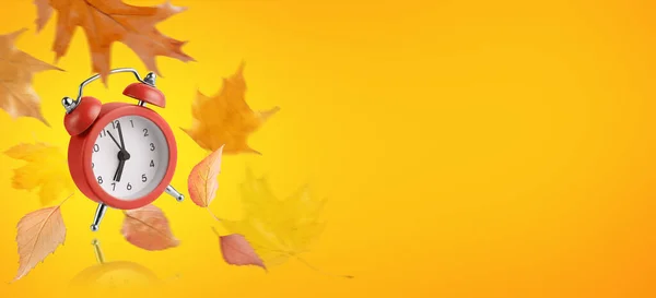 Red alarm clock and flying leaves on orange background. Back to school concept.