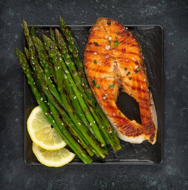 Izgara somon bifteği ve arka planda ızgara tavada kuşkonmaz..