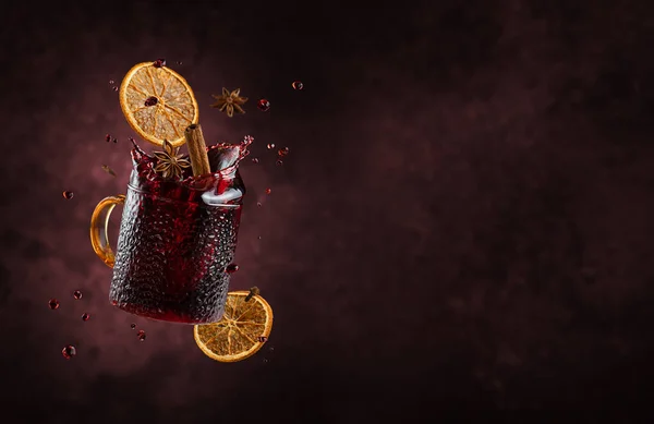 Mulled wine with splashes and flying ingredients on dark background.