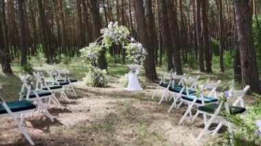 Beautiful bohemian tipi arch decoration on outdoor wedding ceremony venue in pine forest with cones. Chairs, floristic flower compositions of wild flowers. Summer rural wedding. FullHD footage