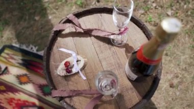Soft focused beautiful wedding rings with champagne glasses on wooden barrel, windy. Slow motion. Wedding details, decor. High quality FullHD footage