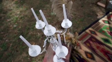 Candles in candle holder, flasks on carpet near bohemian tipi arch decorated on outdoor wedding ceremony venue in pine forest. Boho rustic decor. High quality FullHD footage
