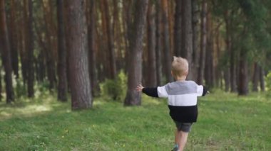 Happy boy runs along country road through a beautiful landscape of green hills. Back view. Childhood. Slow motion. High quality FullHD footage