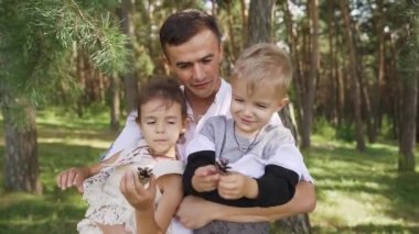 The man holds his son and daughter in his arms in pine forest. A happy family. Walk with your child in the park. Slow motion. High quality FullHD footage