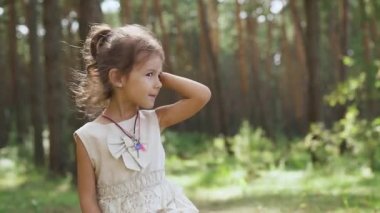 Portrait of charming Caucasian girl talking standing in sunny summer park. Front view happy pretty child resting on spring day outdoors. Leisure and childhood concept. Windy. FullHD footage
