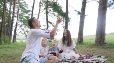 A big happy family has fun in the park in the summer, they sit on the grass and enjoy the marshmallow. Family picnic in nature. Slow motion. High quality FullHD footage
