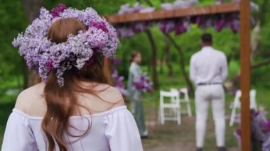 Beautiful Bride in lilac wreath Going Down the Aisle, while Groom Waits at an Outdoors Ceremony Venue Near the waterfall. High quality FullHD footage