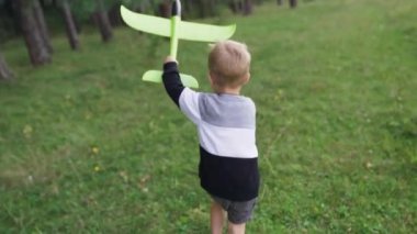 A child boy plays with a toy airplane, runs in the park through a field at sunset and wants to become an astronaut. The kid plays with his favorite toy by airplane in the summer. FullHD footage