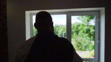 Businessman goes to the window and puts on a jacket. The backlight silhouette. High quality FullHD footage