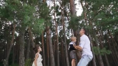 Parent throws their child up. Mother and father are playing with their kids outdoors in the pine forest. Happy family fun in park in summer. Young parent mom and dad play with daughter. Slow motion.