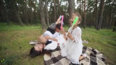 Laughing parents tickling cute kids on picnic blanket wide shot. Parents play with cheerful kids outdoors on summer weekend. Carefree family have fun with two children pampering. FullHD footage