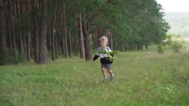 A child boy plays with a toy airplane, runs in the park through a field at sunset and wants to become an astronaut. The kid plays with his favorite toy by airplane in the summer. FullHD footage