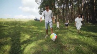Happy family playing a soccer in the park. Group of children in nature playing ball with father and mother. Funny kids playing ball on the grass in summer sunlight. Slow motion. FullHD footage
